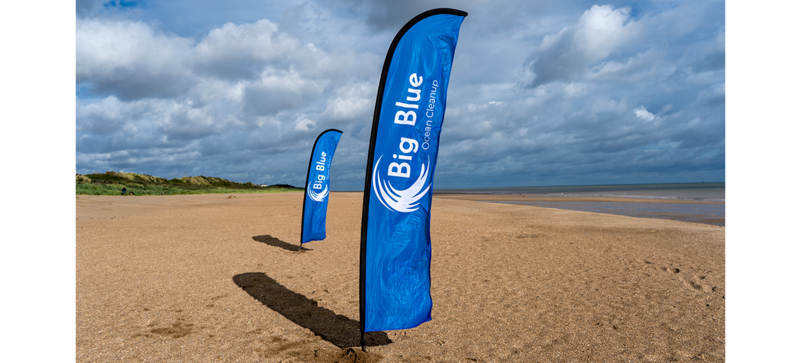 Am Strand sind zwei Strand Flaggen des Big Blue Ocean Cleanup Projekts. 