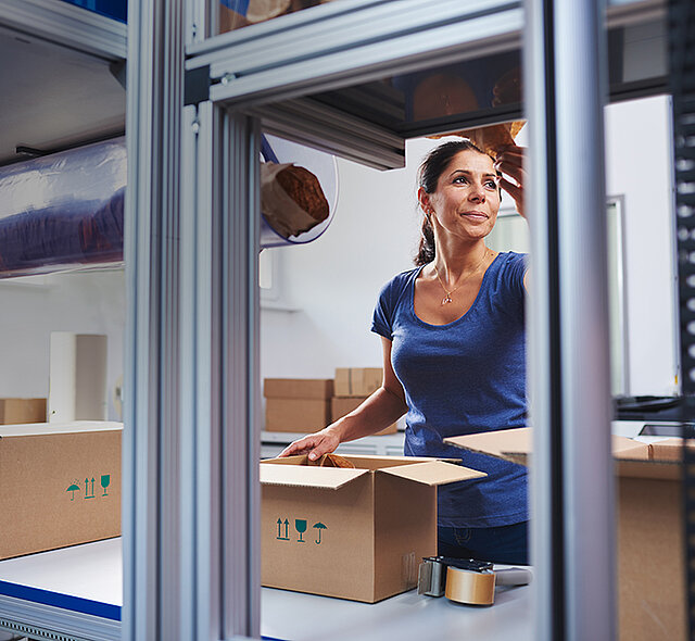 
			Een vrouw verpakt producten bij een verpakkingsstation in een kartonnen doos 